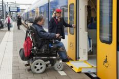 Een NS medewerker verleent assistentie aan een man in een rolstoel