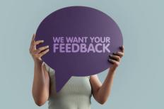 Vrouw houdt een tekstballon voor haar gezicht met daarop de tekst 'We want your feedback'
